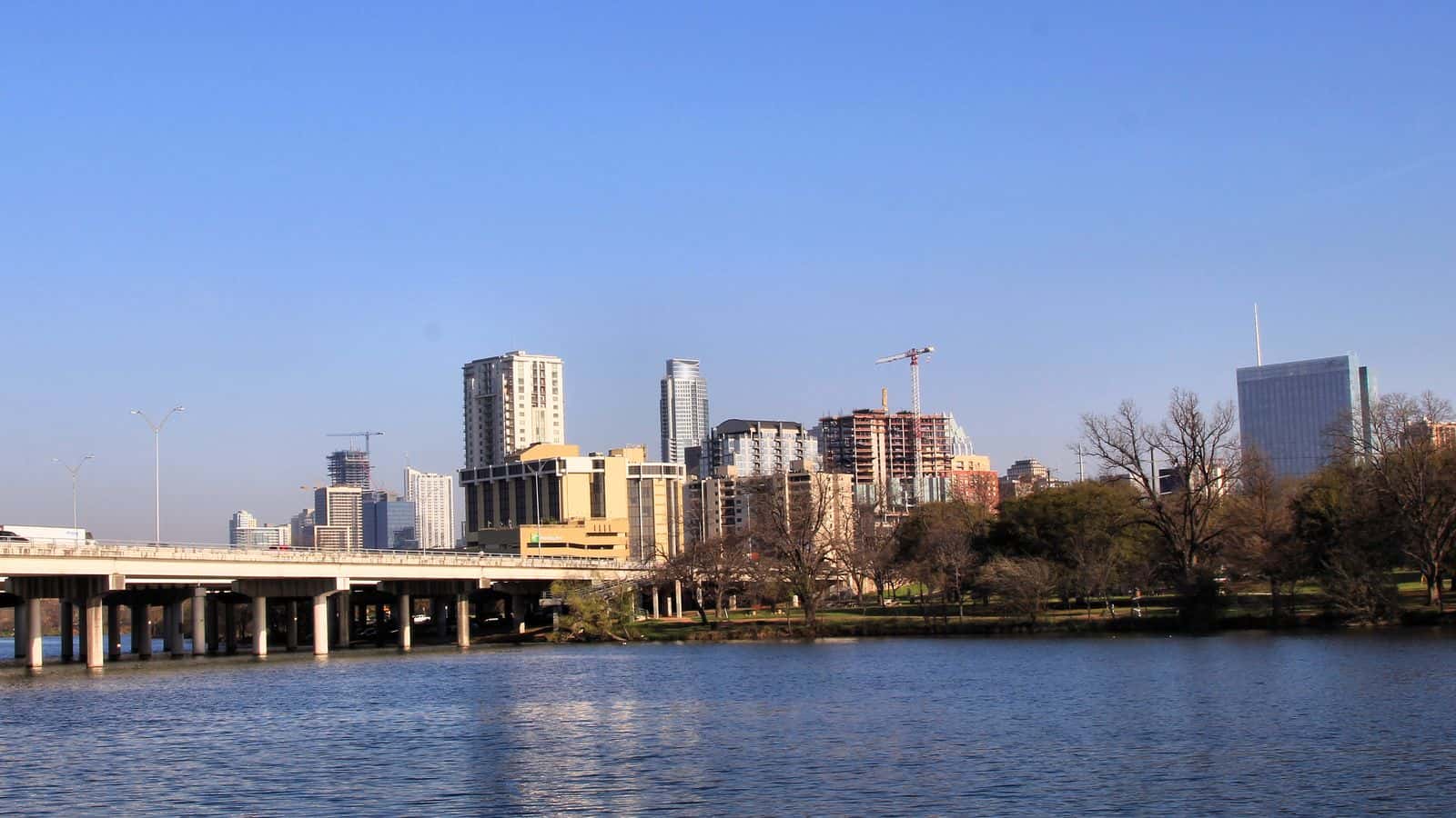 Edificios del centro de Austin al otro lado de Lady Bird Lake, vistos desde la orilla sur al este de la I-35, con el puente de la autopista a la izquierda