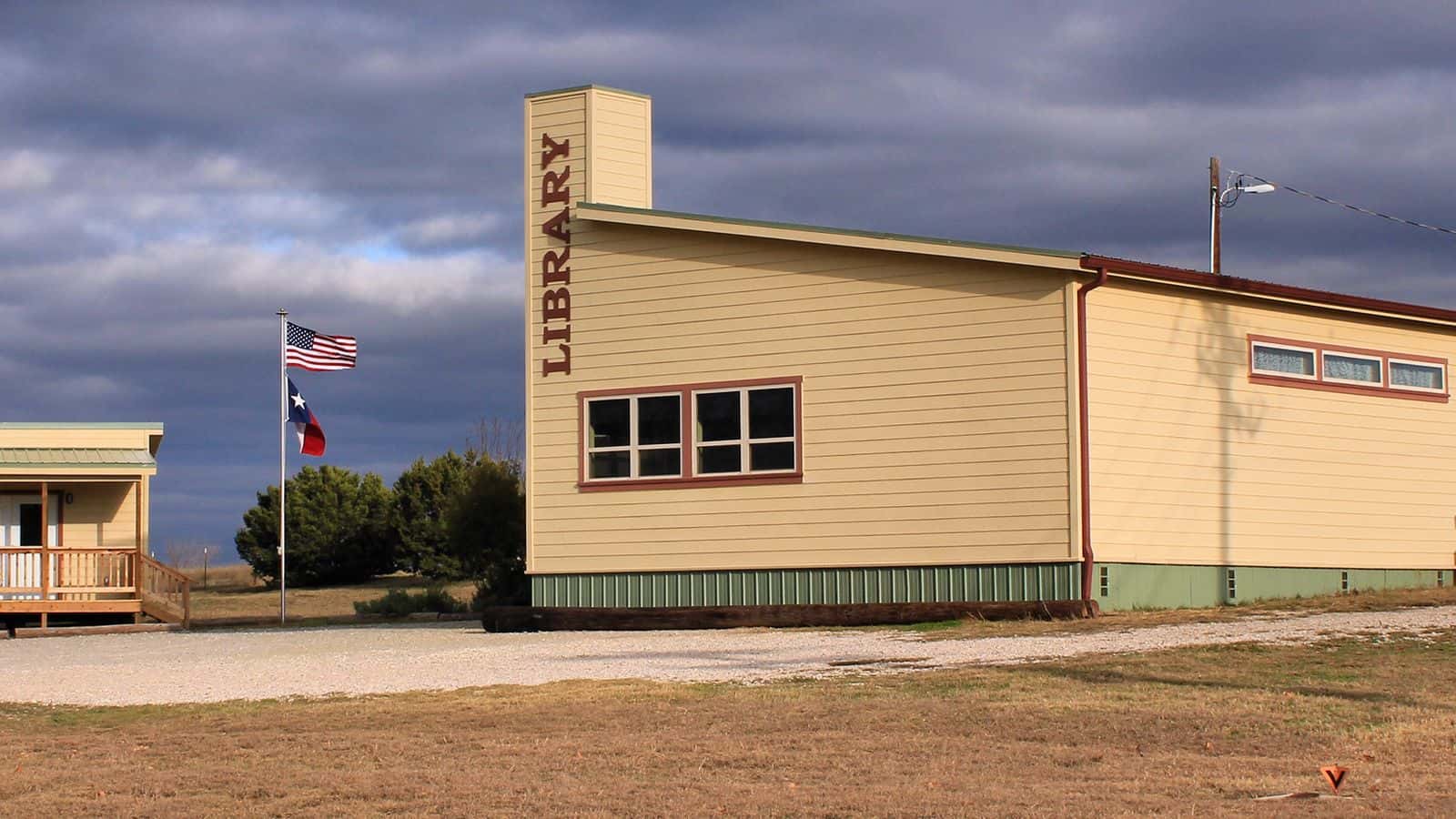 Edificio amarillo claro de la Spicewood Community Library, con la palabra LIBRARY en una torre y banderas de Estados Unidos y de Texas, bajo un cielo nublado